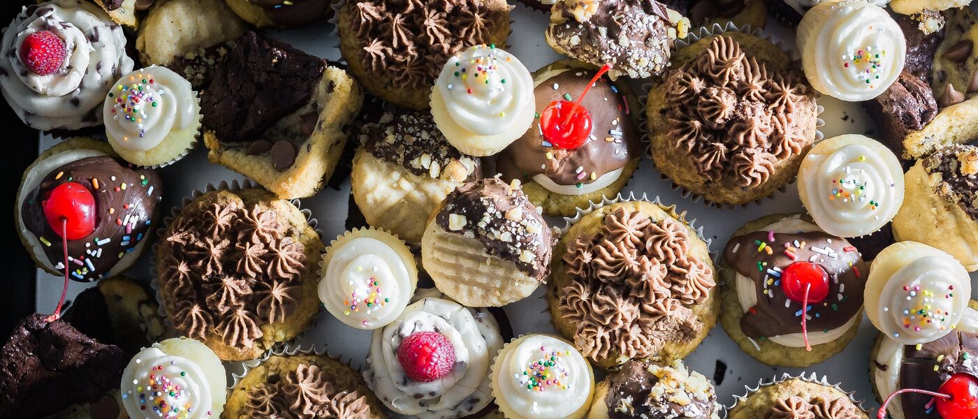 Image of a selection of various cupcakes and muffins with frosting, sprinkles and cherries.